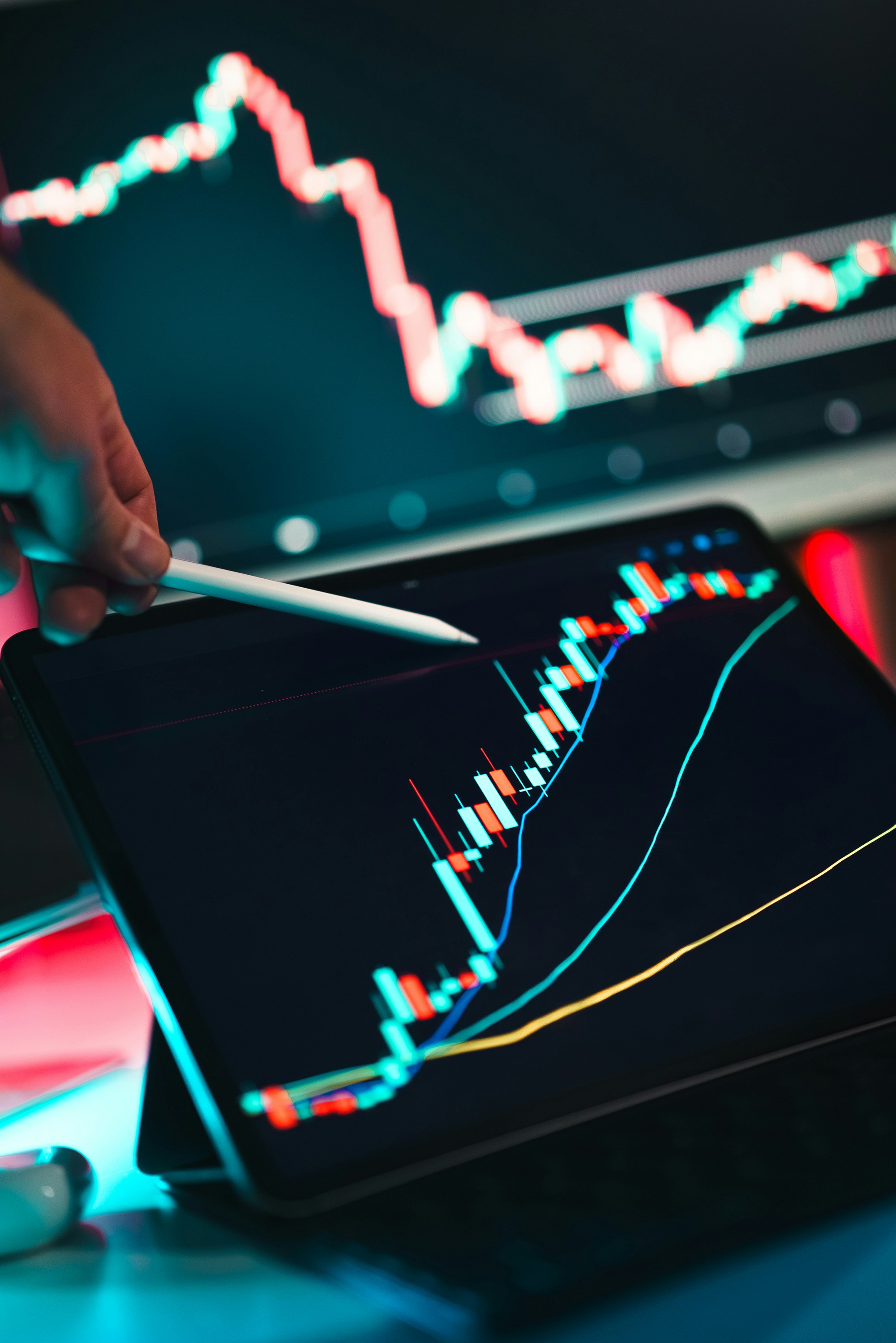 Une main tenant un stylet pointant vers un graphique financier sur un écran, montrant des barres et des lignes de tendance colorées.