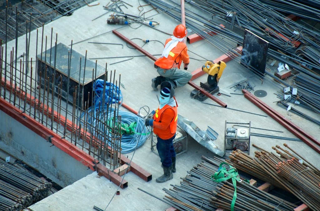 Des ouvriers en chantier, portant des casques et des vêtements de sécurité, travaillent sur des structures en béton et des barres d'acier.