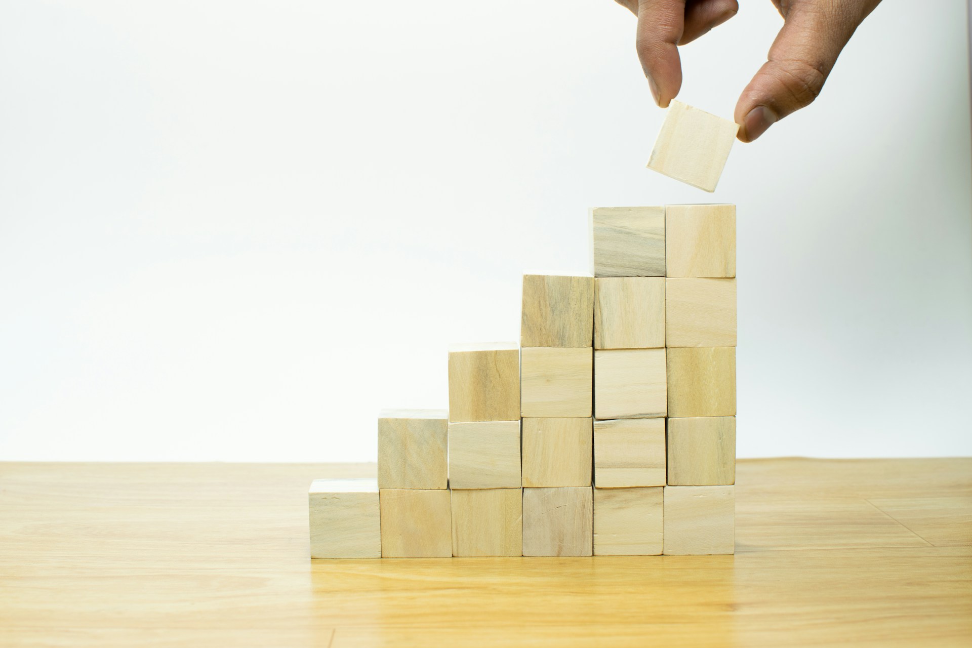 Une main plaçant un cube en bois au sommet d'une structure de cubes formant un escalier, symbolisant la croissance et le développement.