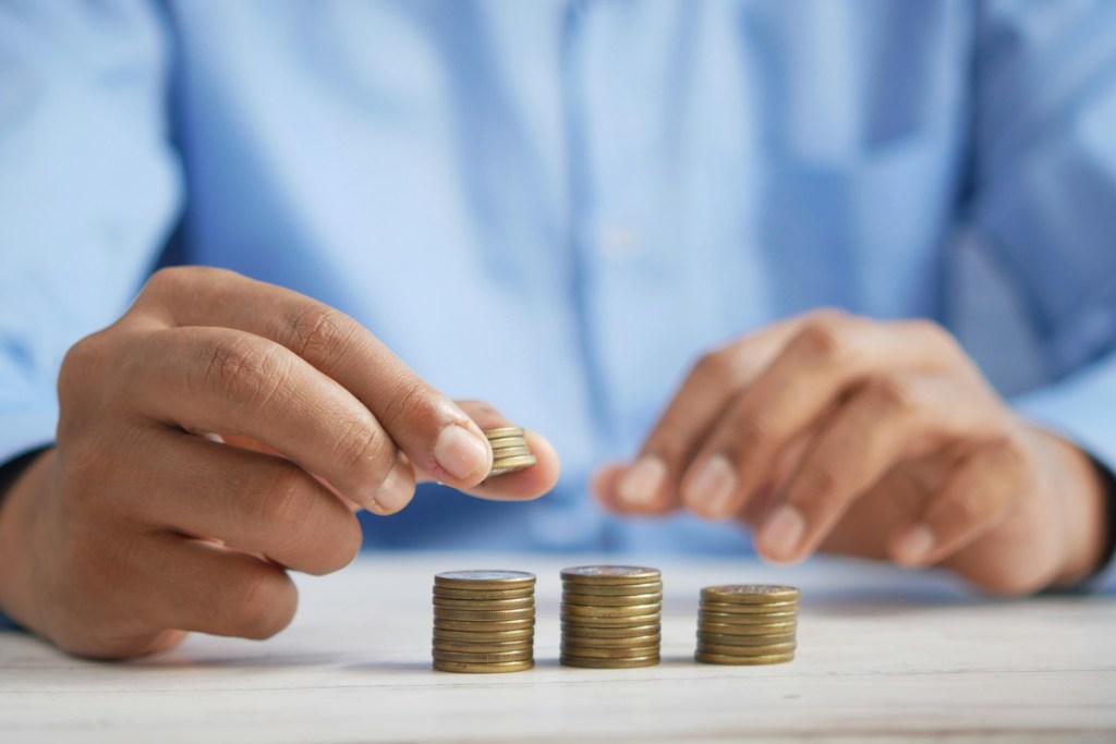 Un homme en chemise bleue empile des pièces de monnaie sur une table en bois, illustrant la gestion financière.